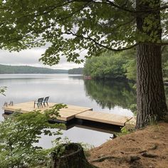 two chairs on a dock in the middle of a body of water with trees around it