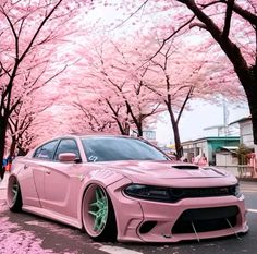 the pink car is parked on the side of the road with cherry blossom trees in the background