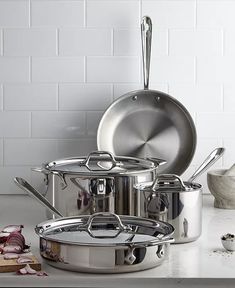 stainless steel pots and pans on a white countertop with garlic next to them