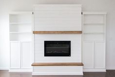 an empty room with white painted walls and built - in bookshelves, including a fireplace