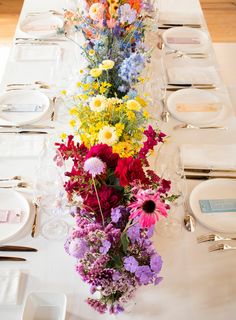 a long table is set with flowers and place settings for the guests to sit at