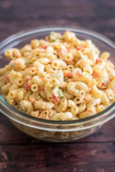 a glass bowl filled with macaroni salad on top of a wooden table next to a fork