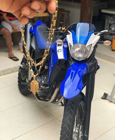 a blue motorcycle parked on top of a tile floor next to a person holding a chain