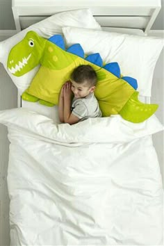 a young boy laying in bed under a green and blue pillow with an alligator on it