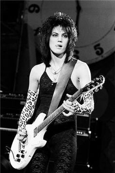 a woman holding a guitar while standing next to a clock