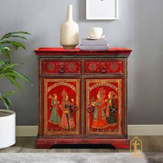 an ornate red cabinet with paintings on the front and sides, along with a potted plant