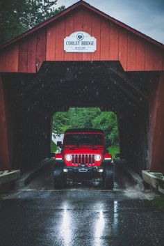 a red jeep is parked in front of a covered bridge on a rainy day,