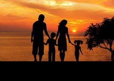 a family is silhouetted against an orange sunset over the ocean