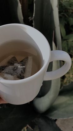 a hand holding a white cup filled with tea and some sort of substance in it