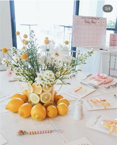 a vase filled with lemons and daisies sitting on top of a white table