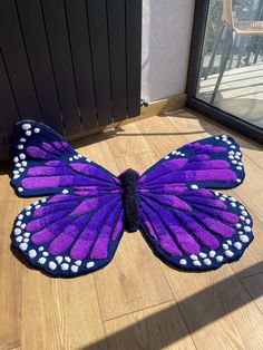 a large purple butterfly sitting on top of a hard wood floor next to a window