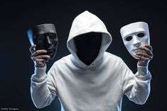 a person wearing a white hoodie holding two masks in front of their face with both hands