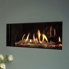 a wall mounted fireplace with flames burning in the dark and white flowers sitting on top of it