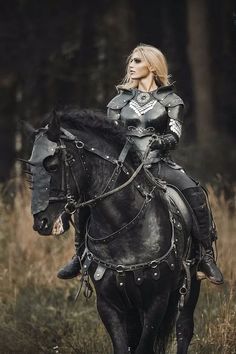 a woman in armor riding on the back of a black horse through a field with tall grass