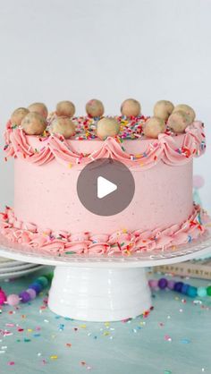 a pink frosted cake with sprinkles and cookies on top is shown