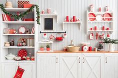 a kitchen decorated for christmas with red and white dishes on shelves, wreaths and other holiday decorations