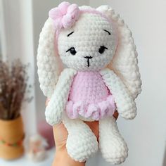 a small crocheted white and pink stuffed animal with a pink dress on it's chest