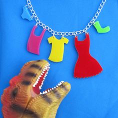 a toy dinosaur with clothes hanging from it's mouth on a chain necklace that is attached to a blue background