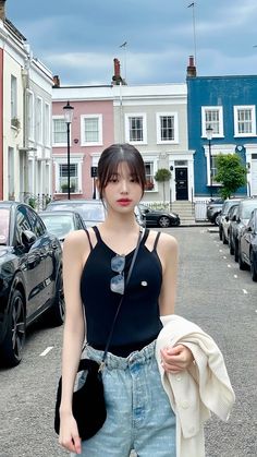 a woman standing in the middle of a street with cars parked on both sides and buildings behind her