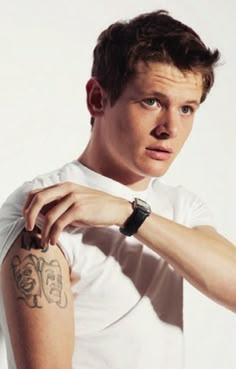 a man with a tattoo on his arm holding onto a watch and looking at the camera