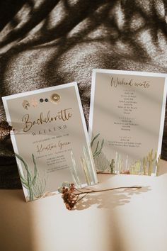 two wedding cards sitting on top of a table with succulents and greenery