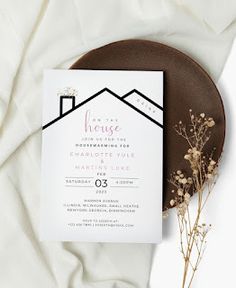 a white and black wedding card on top of a plate next to some dried flowers