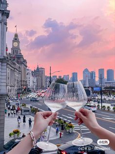 two people holding wine glasses in front of a cityscape at sunset with the sun setting