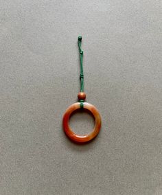 an orange and brown ring hanging from a green string on a gray surface with a white background