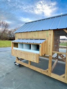 a large wooden chicken coop on wheels in front of a building with a metal roof