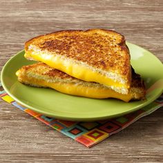 a grilled cheese sandwich on a green plate with a colorful napkin and wooden table