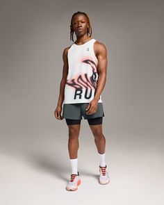 a man standing in front of a gray background wearing shorts and a white tank top