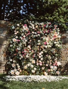 an arrangement of pink and white flowers on display in front of a brick wall with grass