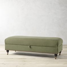 an upholstered bench with wooden legs and nail - tipped feet, on a wood floor