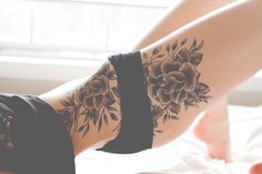 a woman's legs with tattoos on them sitting on top of a bed next to a window