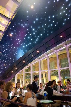 a group of people sitting at tables in a restaurant with lights on the ceiling above them