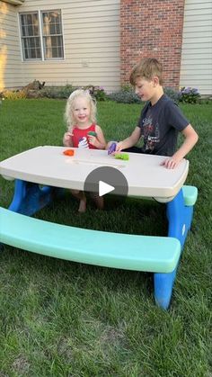 two children sitting at a table outside in the grass, playing with blocks and toys