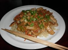 a white plate topped with chicken and rice next to chopsticks on a table