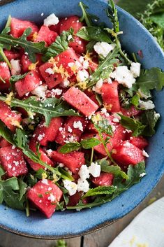 watermelon salad with feta cheese and herbs in a blue bowl on a wooden table