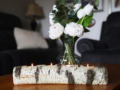 a candle holder made out of birch logs with white flowers in the vase behind it