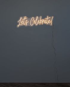 a neon sign that says let's celebrate hanging from the ceiling in front of a gray wall