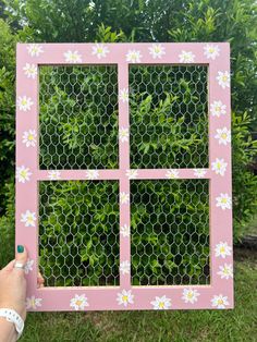 a person holding up a pink frame with white flowers on it and green grass in the background