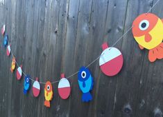 some paper fish are hanging from a line on a wooden fence with other items attached to it