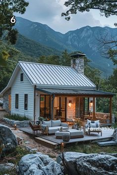 a small white cabin in the mountains with a porch and seating area for people to sit on