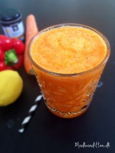 an orange drink in a glass next to some vegetables