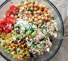 a glass bowl filled with different types of vegetables and chickpeas on top of a table