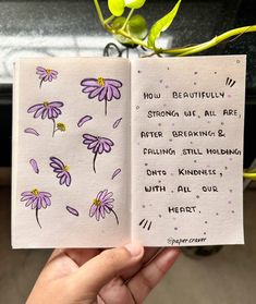 a hand holding an open book with purple flowers on it and the words how beautifully strong we are