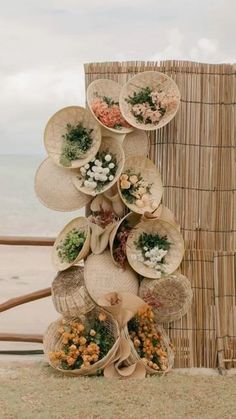 a stack of baskets with flowers on the beach in front of a bamboo fence and water