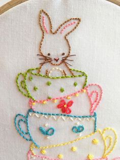 a close up of a embroidery on a piece of cloth with a bunny in a teacup