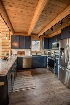 a kitchen with blue cabinets and stainless steel appliances in the cabin style home that has wood paneling on the ceiling