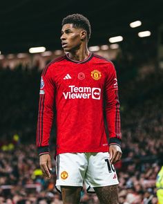 a man standing on top of a soccer field wearing a red shirt and white shorts